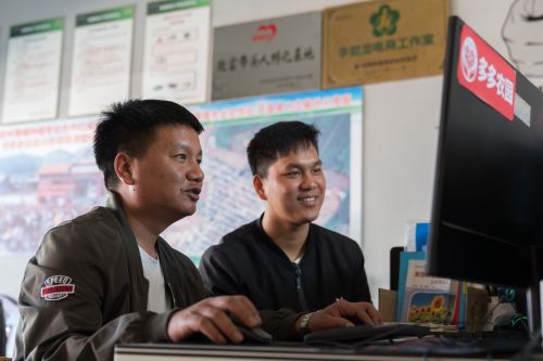 ▲李能龙（左）正在跟合作社社员肖小双（右）探讨拼多多店铺的运营。 （穆功 摄）

