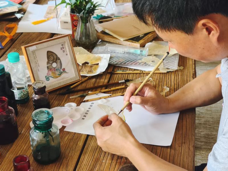 凌源皮影戏县级非遗传承人张佐飞正在给以玉猪龙为形象的皮影工艺品上色